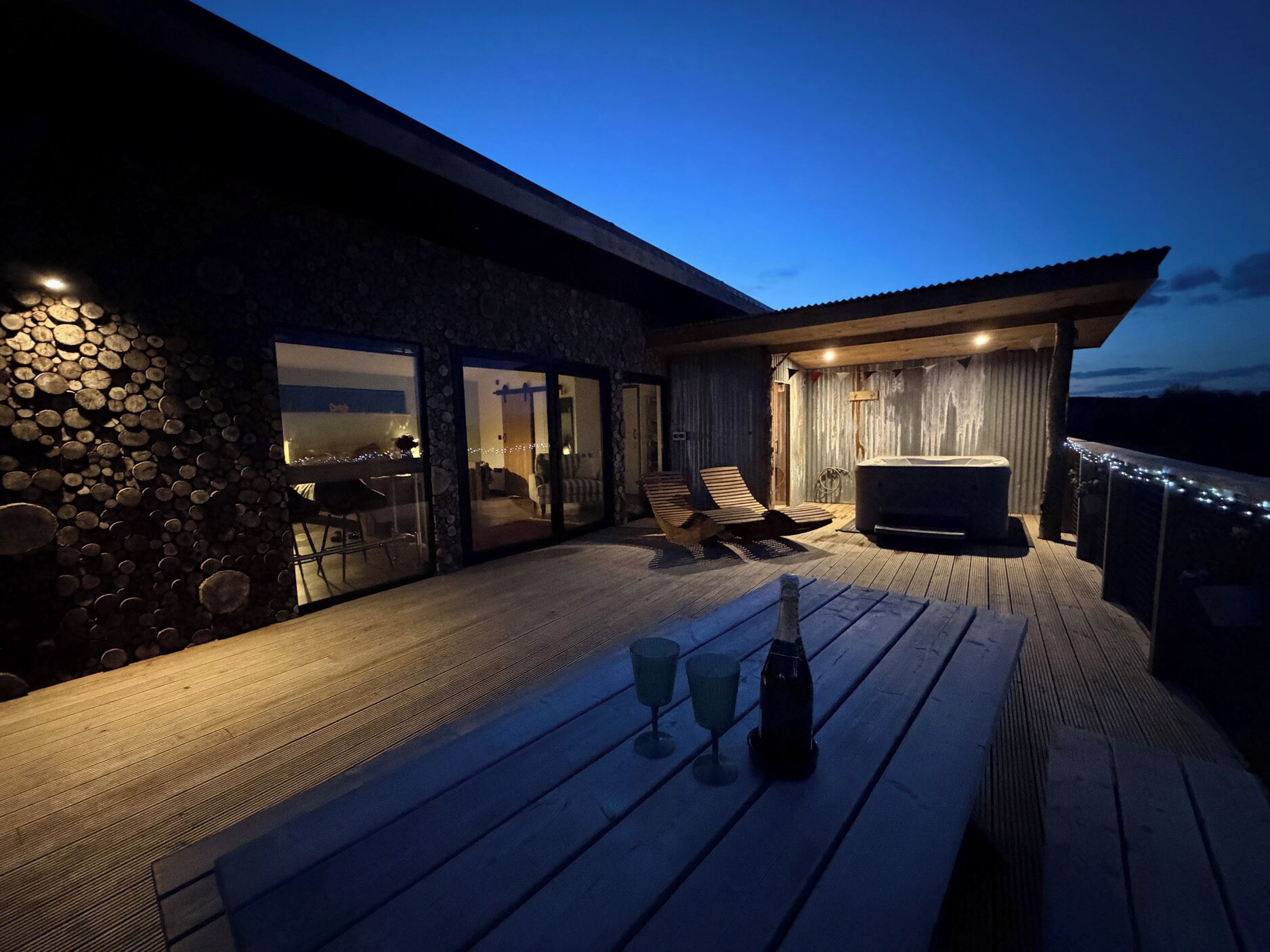 Une terrasse en bois avec des chaises longues, un jacuzzi et un mur en pierre.