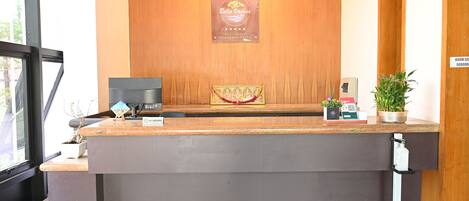 A reception desk with a wooden backdrop, a framed certificate, a coffee machine, and a potted plant.