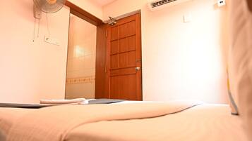 A hotel room with a bed, a standing fan, an air conditioning unit, and a wooden door.