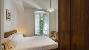 A bedroom with a wooden bed, a nightstand, a chair, and a window with curtains.