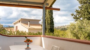 A white table with a bowl of fruit on a balcony with a view of a house and trees. - Casa degli Ulivi con terrazza by Wonderful Italy (Siracusa)