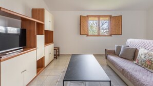 A modern living room with a flat-screen TV, wooden cabinets, a sofa, and a large window. - Casa degli Ulivi con terrazza by Wonderful Italy (Siracusa)