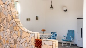 Een stenen muur, een tafel met een fruitschaal, een blauwe stoel en een hanglamp.