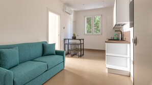 A modern, minimalistic living space with a teal sofa, a small table with a plant, and a kitchenette area. - Crispi Suite in Palermo by Wonderful Italy (Palermo)