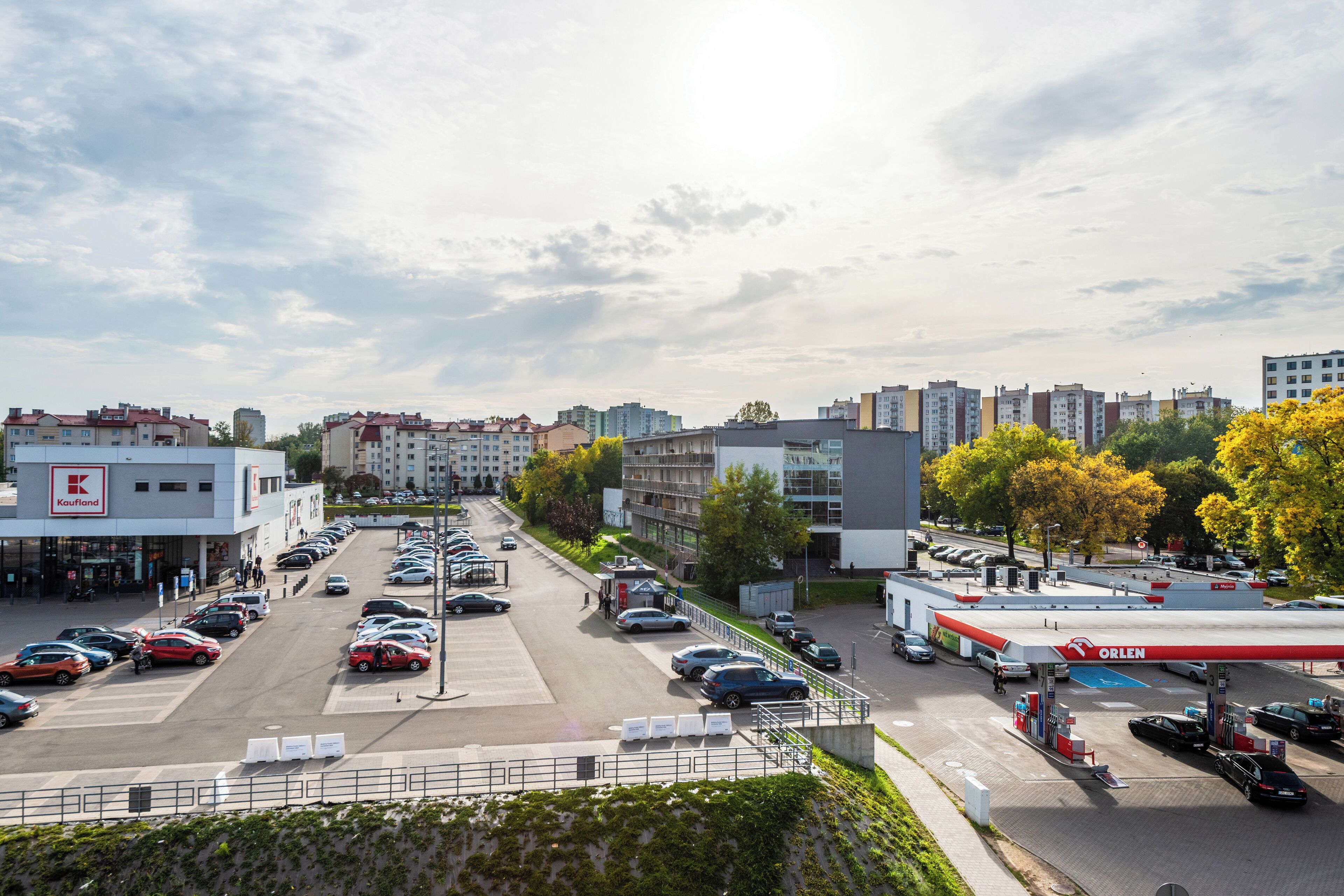 A parking lot with multiple cars, a gas station, and surrounding buildings.