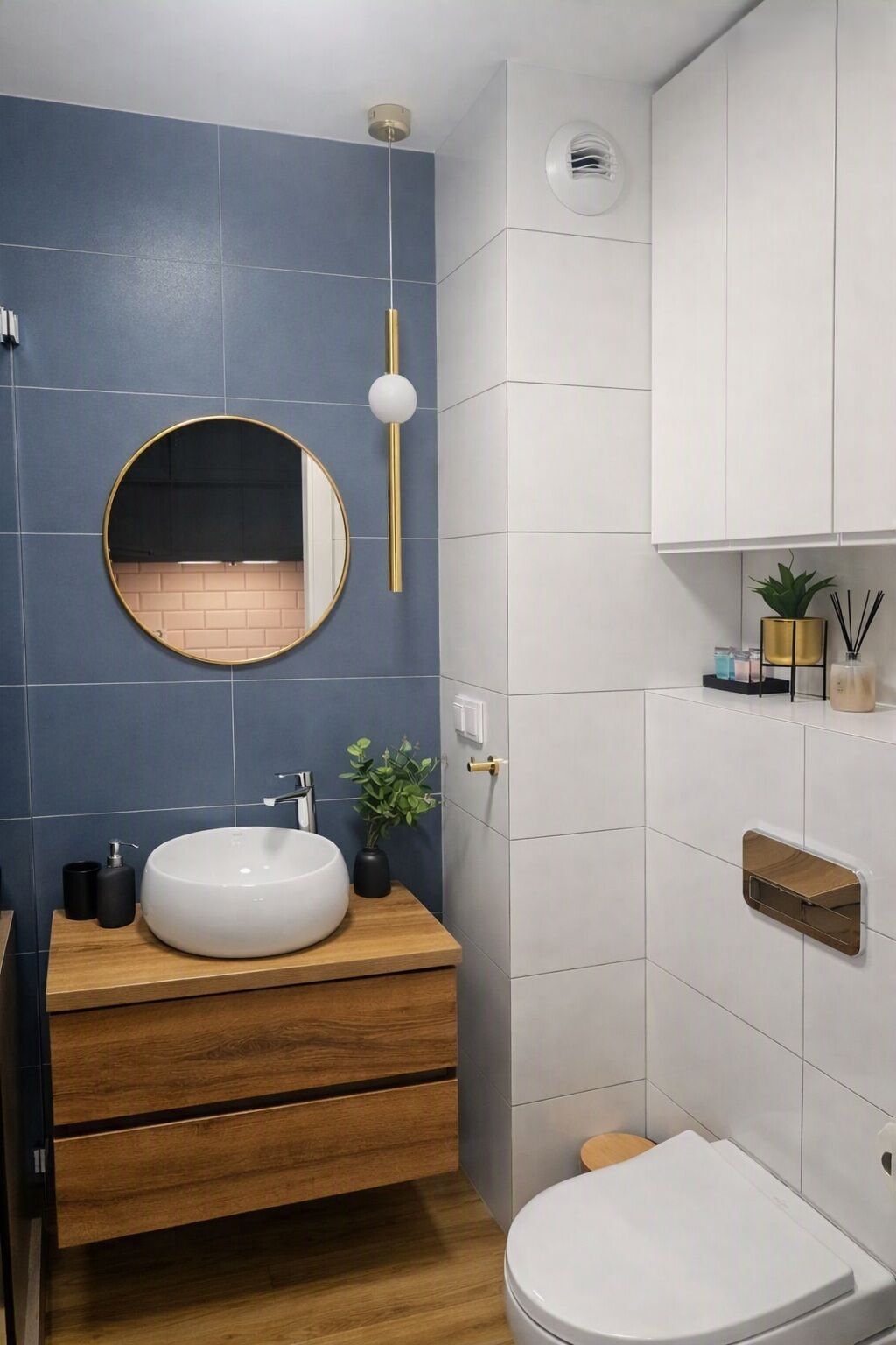 A modern bathroom with a round mirror, white sink, wooden vanity, and a white toilet.