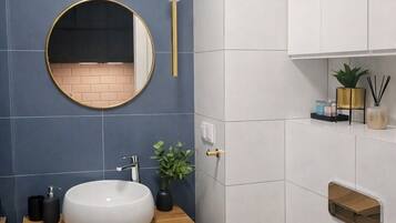 A modern bathroom with a round mirror, white sink, wooden vanity, and a white toilet.