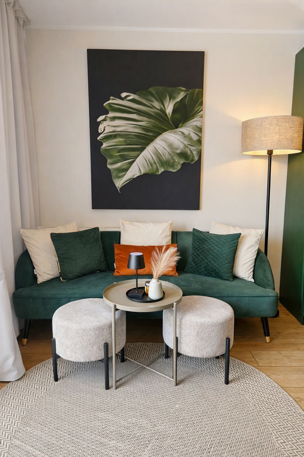 A living room with a green sofa, two round tables, and a large plant artwork on the wall.