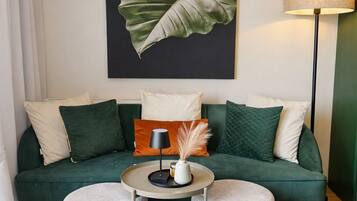 A living room with a green sofa, two round tables, and a large plant artwork on the wall.