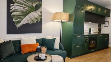 A modern living room with a green sofa, a small round table, and a kitchen with green cabinets.