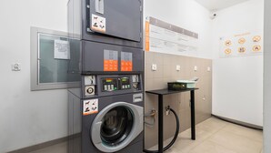 Un cuarto de lavandería con lavadoras apiladas, un panel de control y carteles informativos en las paredes.