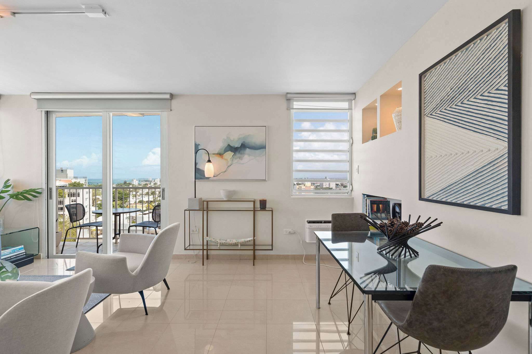 Ein modernes Wohnzimmer mit einem Glastisch, weißen Stühlen, einer Couch und einem Balkon mit Blick auf die Stadt.
