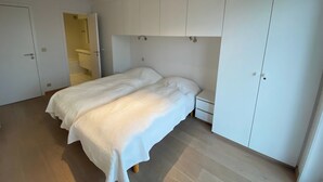 A bedroom with a bed, a wardrobe, and a bathroom visible through an open door. - Seafront Palm Beach Stay (Knokke-Heist)