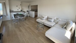 A modern living room with a sofa, a dining area with a table and chairs, and a kitchen in the background. - Apartment in Knokke Near the Beach (Knokke-Heist)