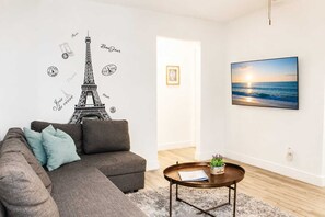 Ein Wohnzimmer mit einer Couch, einem Couchtisch, einem an der Wand befestigten Bild von einem Sonnenuntergang und einer Wandsticker-Darstellung des Eiffelturms.