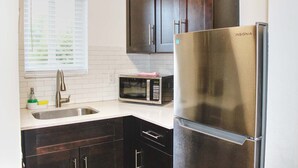 A kitchen with dark wooden cabinets, a stainless steel refrigerator, a microwave, and a sink with a window above it.