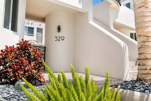 Un bâtiment moderne, orné d’un grand chiffre « 329 » sur le mur, avec un escalier et un jardin bien entretenu, où l’on trouve des arbustes aux feuilles rouges et des plantes vertes.