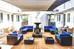 An outdoor seating area with blue sofas and wicker furniture, a central fire feature, and an 'EXIT' sign on the walls.