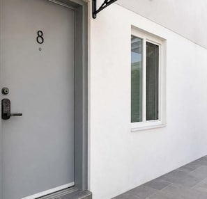 Una puerta moderna con teclado numérico, una ventana con persianas y una pared exterior limpia.