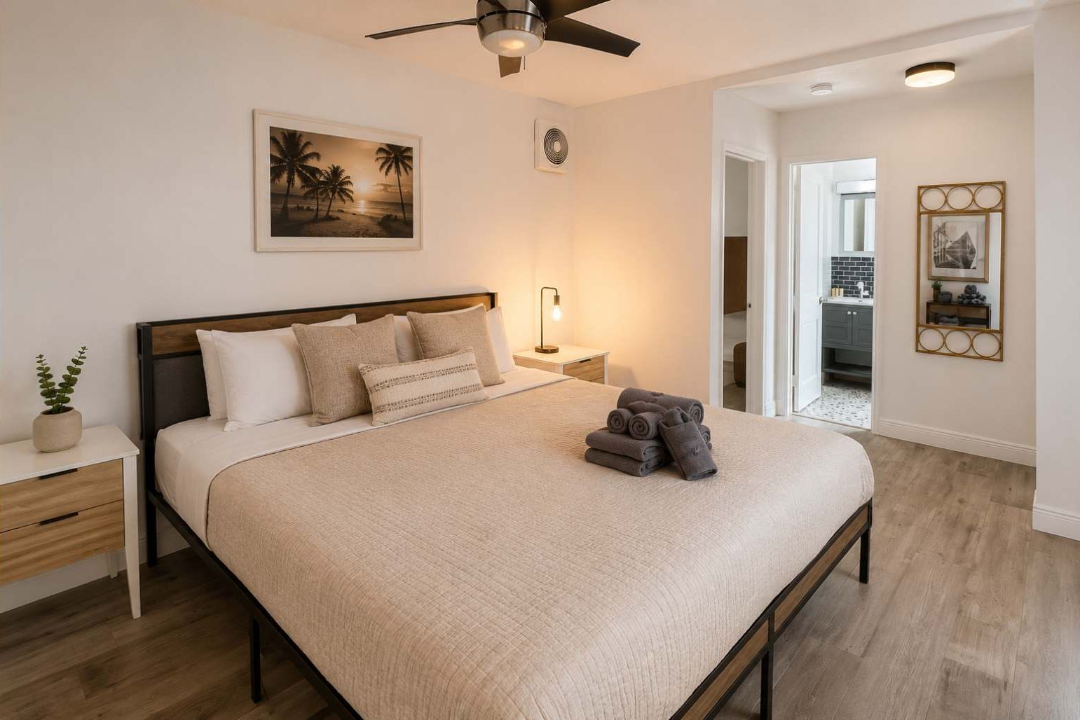Une chambre à coucher avec un lit, des tables de chevet, un ventilateur de plafond, un tableau et une vue sur une autre pièce.