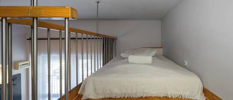 A bedroom with a wooden floor, a white bed with a white throw, and a metal railing.