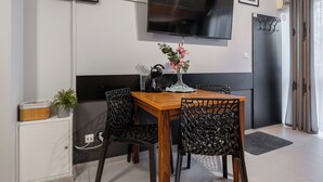 Ett modernt matområde med ett träbord och svarta metallstolar, en platt-TV som är monterad på väggen och en liten krukväxt på sidobordet.