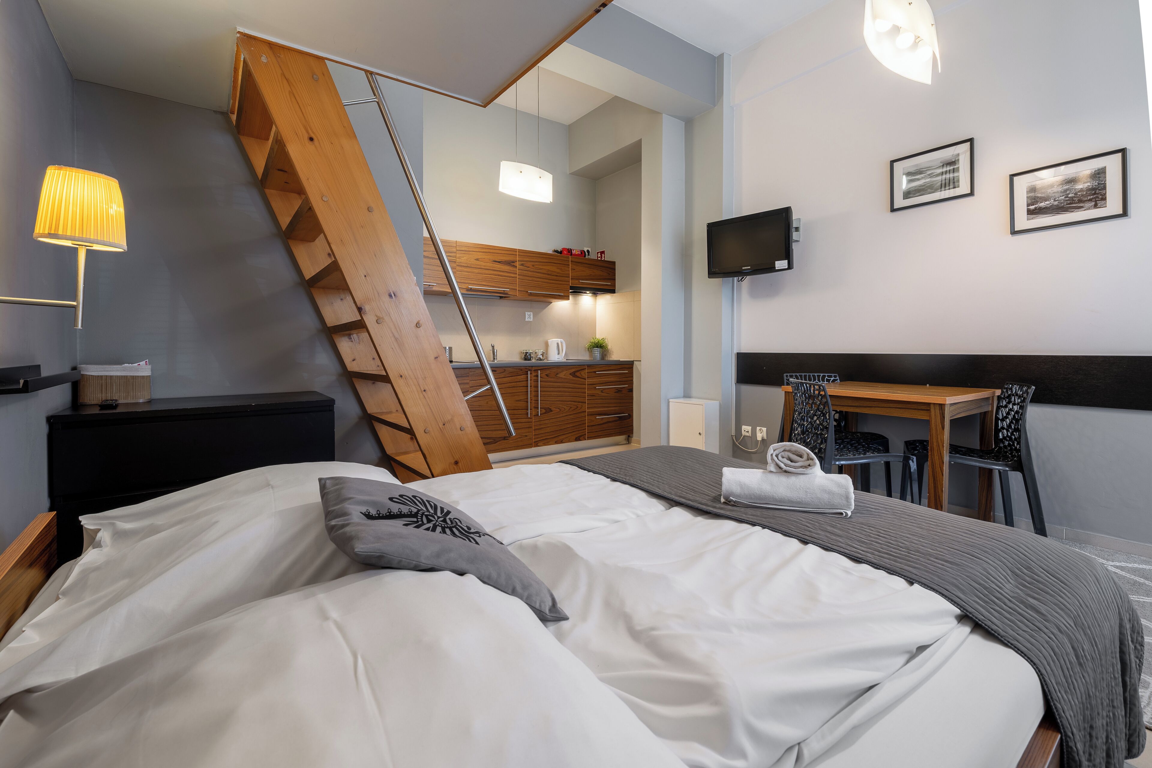 A bedroom with a bed, a desk, a chair, a TV, and a staircase.