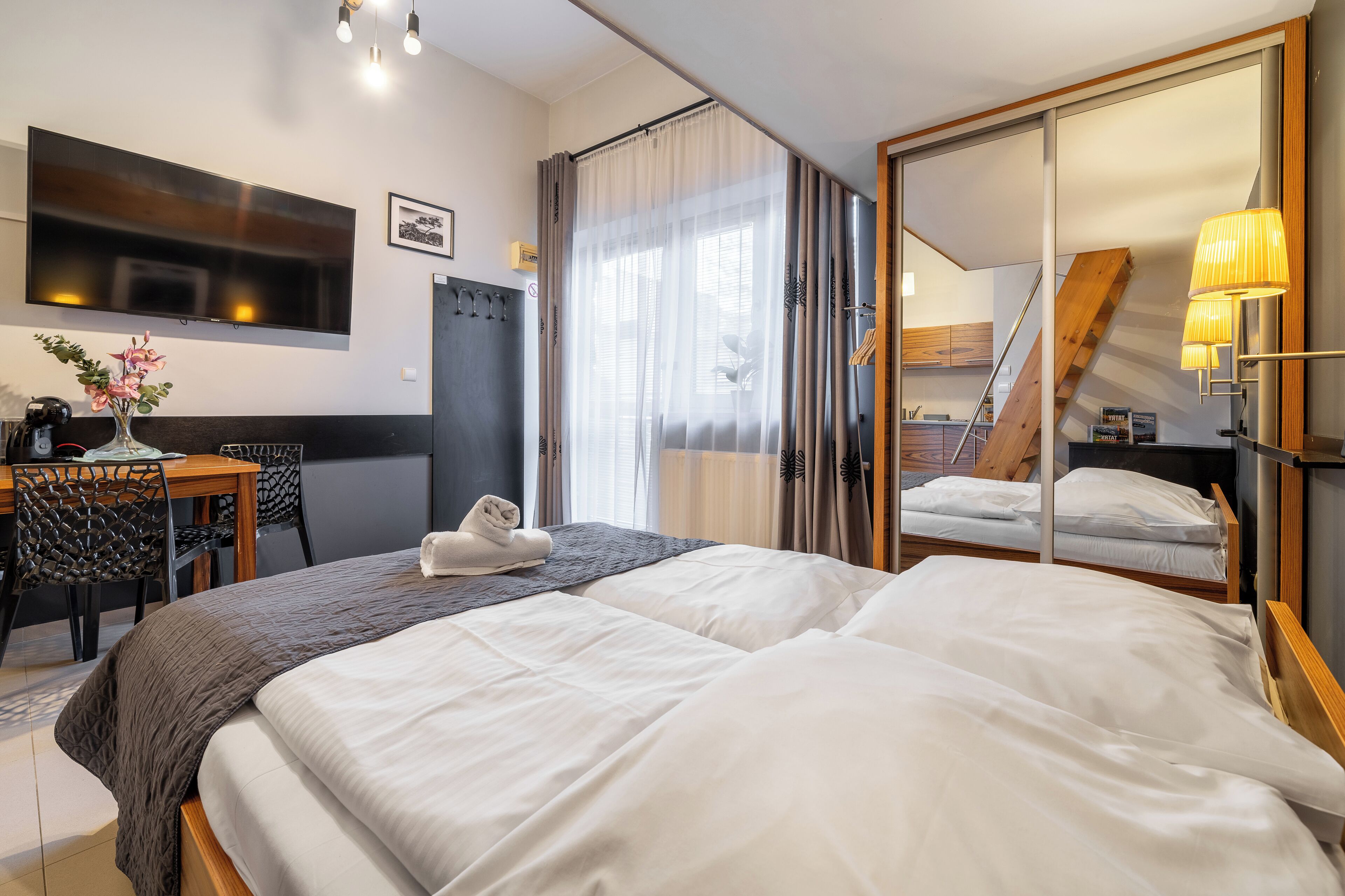 A hotel room with a large bed, a desk with chairs, a TV, and a mirror.