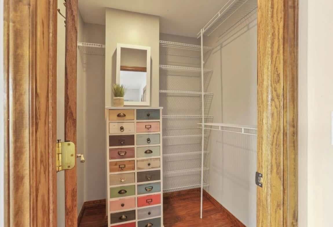 A narrow hallway with a wooden door on the left, a white storage unit with multiple drawers on the right, and a metal shelving unit against the wall.