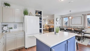 Une cuisine moderne avec des meubles blancs, un îlot central bleu et un coin repas comprenant une table et des chaises.