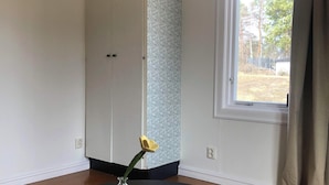 A room with a round black table, a vase with a yellow flower, a remote control, a white wardrobe, a patterned wall, and a window with curtains. - Ölrun Stuga (Hammarstrand)