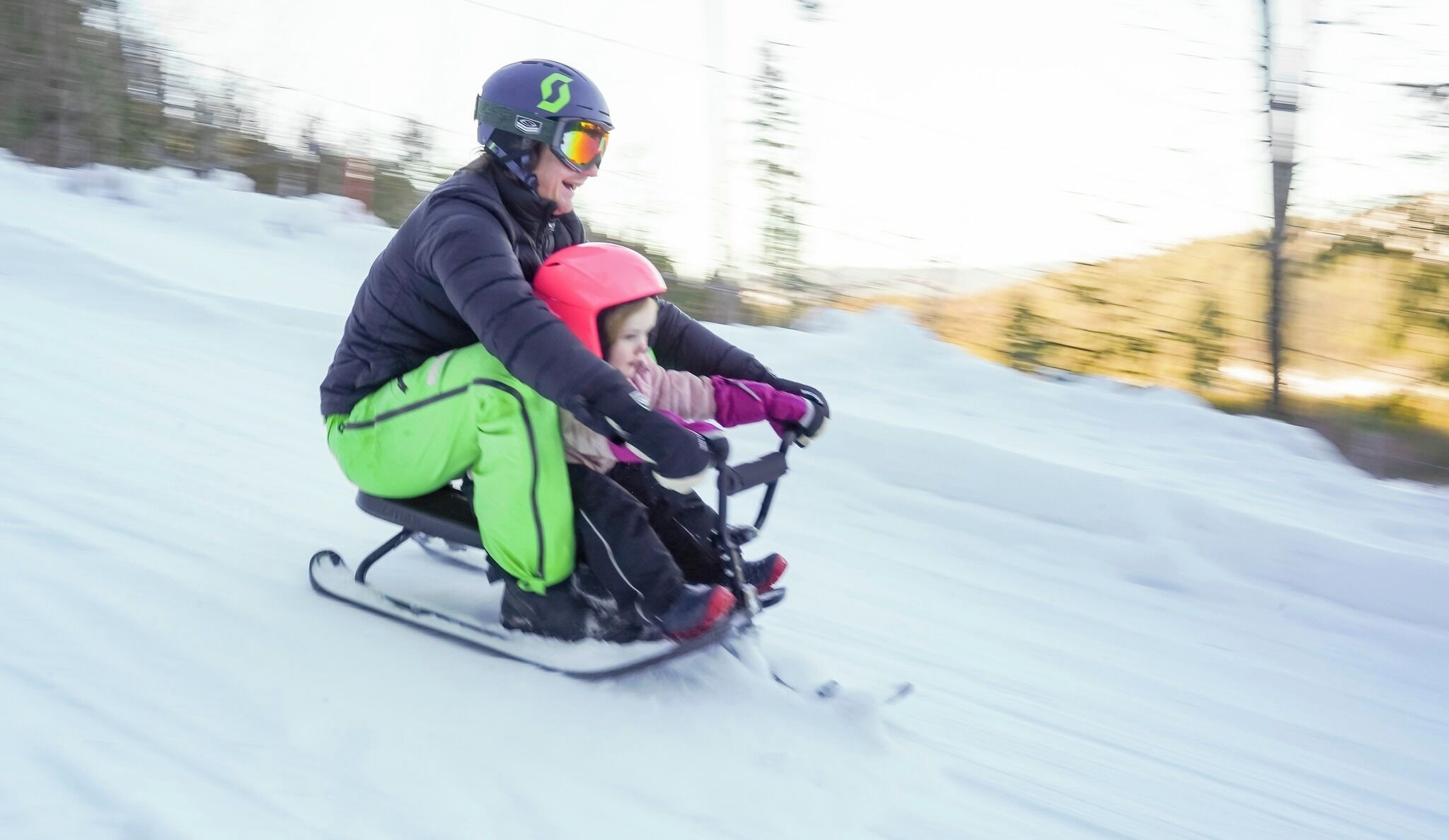 A person and a child on a sled moving down a snowy slope.