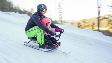 A person and a child on a sled moving down a snowy slope.