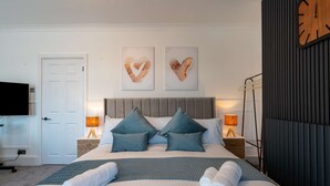 A modern hotel room with a large bed, two heart-shaped wall art pieces, a flat-screen TV, and a clock on the wall.