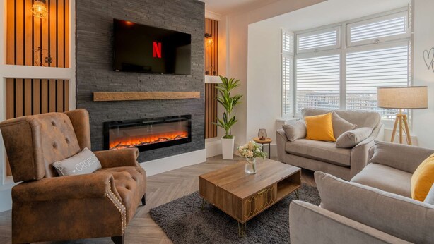 A modern living room with a fireplace, a flat-screen TV mounted above it, and a comfortable seating area with a sofa and armchairs.