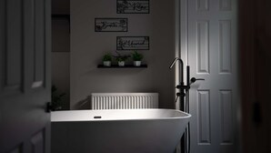 A bathroom with a freestanding bathtub, a white radiator, and three wall-mounted signs reading "Soak," "Relax," and "Breathe."
