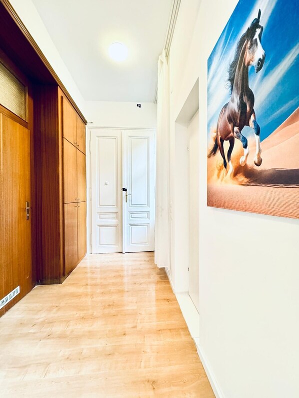 A hallway with wooden flooring, white doors, and a large painting of a horse on the wall.