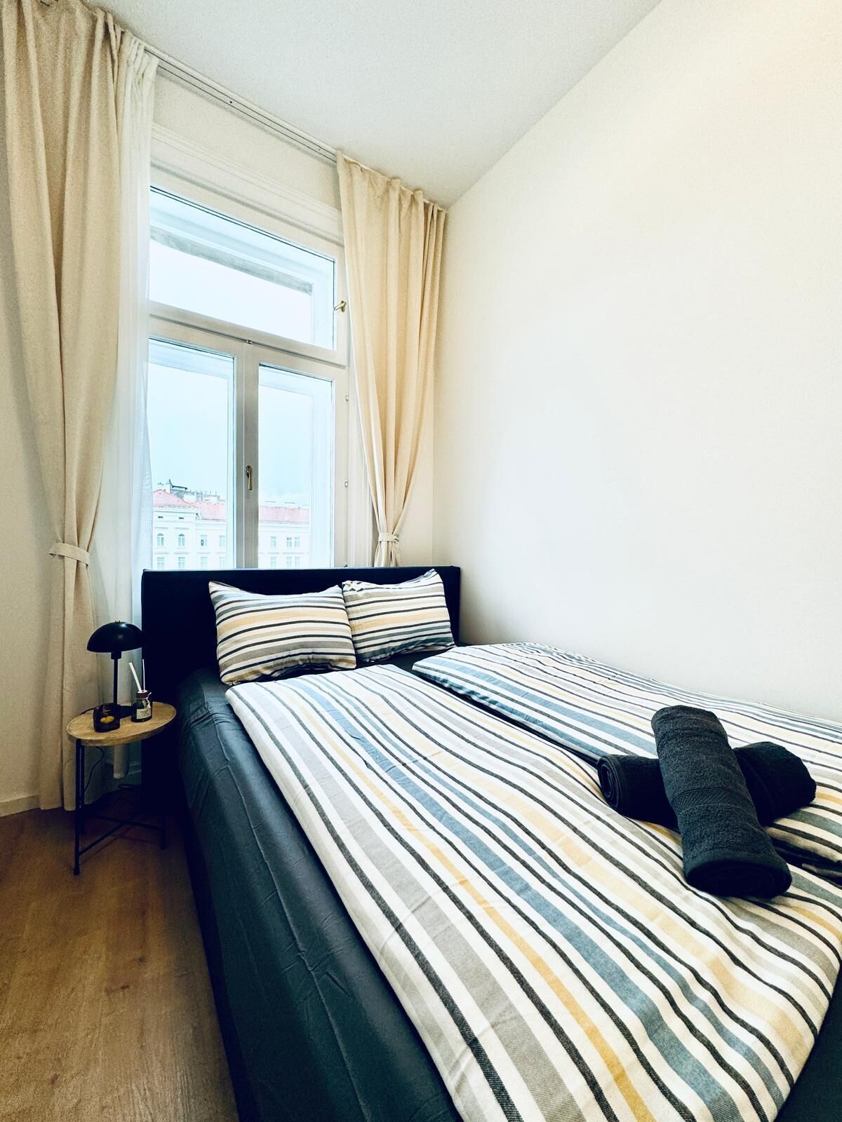 A bedroom with a bed, a nightstand, a lamp, and a window with curtains.