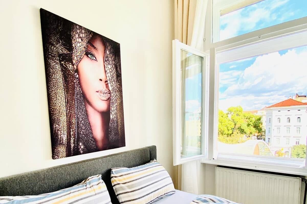 Een hotelkamer met een bed, gestreept beddengoed, een groot raam met uitzicht op gebouwen, en een schilderij aan de muur.