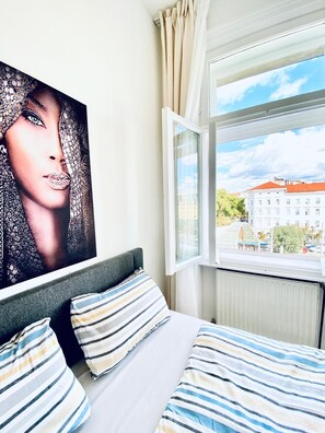 A bedroom with a bed, striped pillows, a large window, and a view of buildings outside.