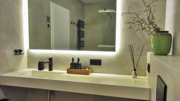 A modern bathroom with a large mirror, a sink with a wooden tray, a green vase, and a toilet with a towel.