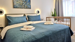 A bedroom with a large bed, a headboard, a painting, and a window with curtains.