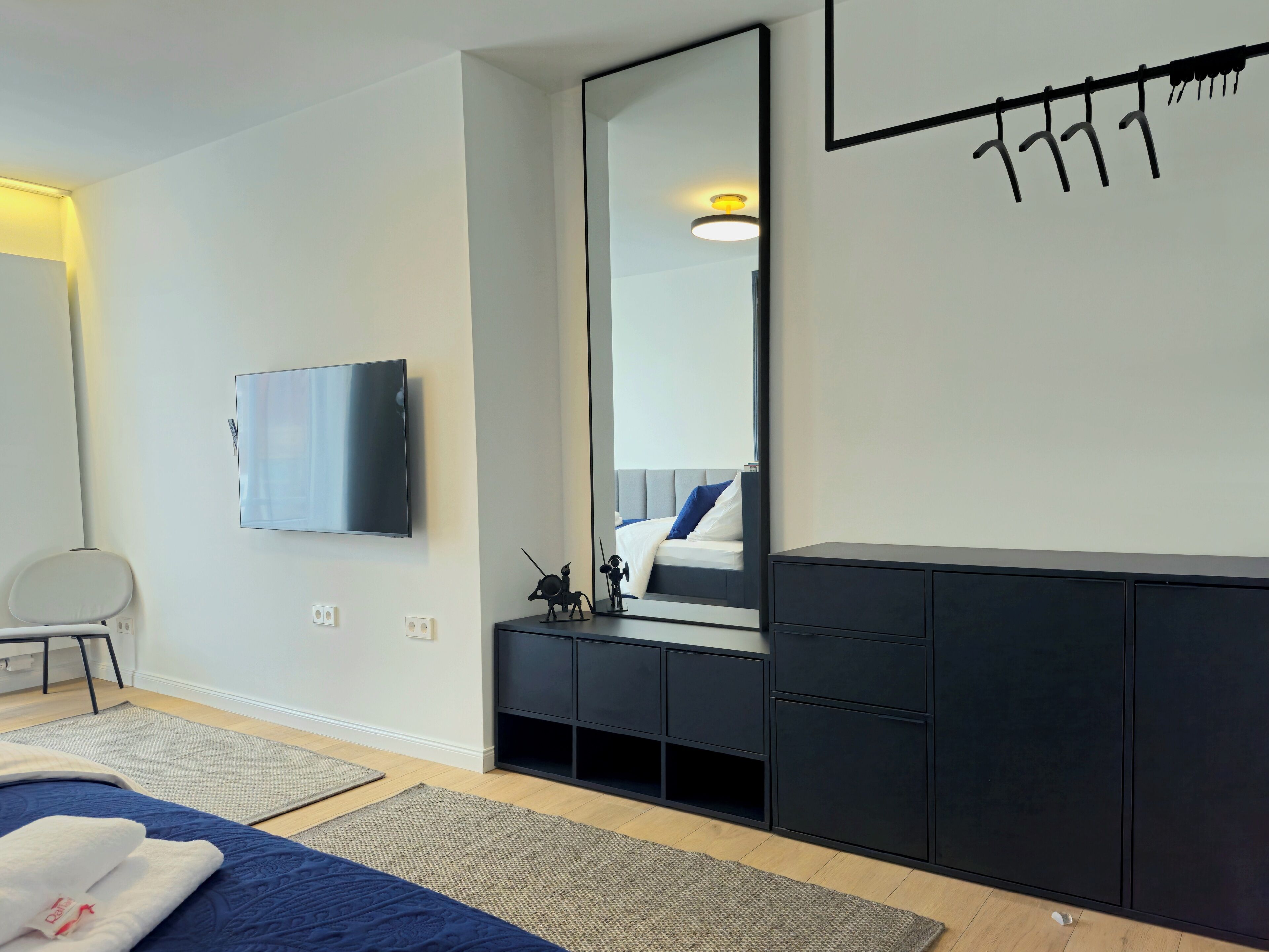 Een moderne slaapkamer met een groot bed, een flatscreen televisie, een garderobe en een spiegel.