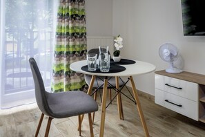 Een moderne eetruimte met een ronde tafel, twee stoelen, een wit kastje en een staande ventilator.