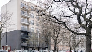 Een meerlaags gebouw met balkons, geparkeerde auto's en kale bomen.