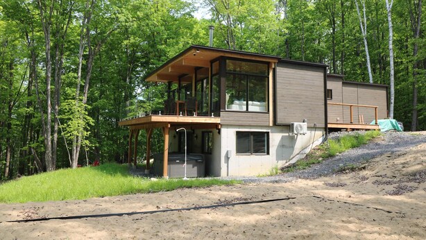 A modern two-story cabin with a balcony, surrounded by a forest. - Lake, Spa & Game Room | Le Havre du Voyageur (La Minerve)