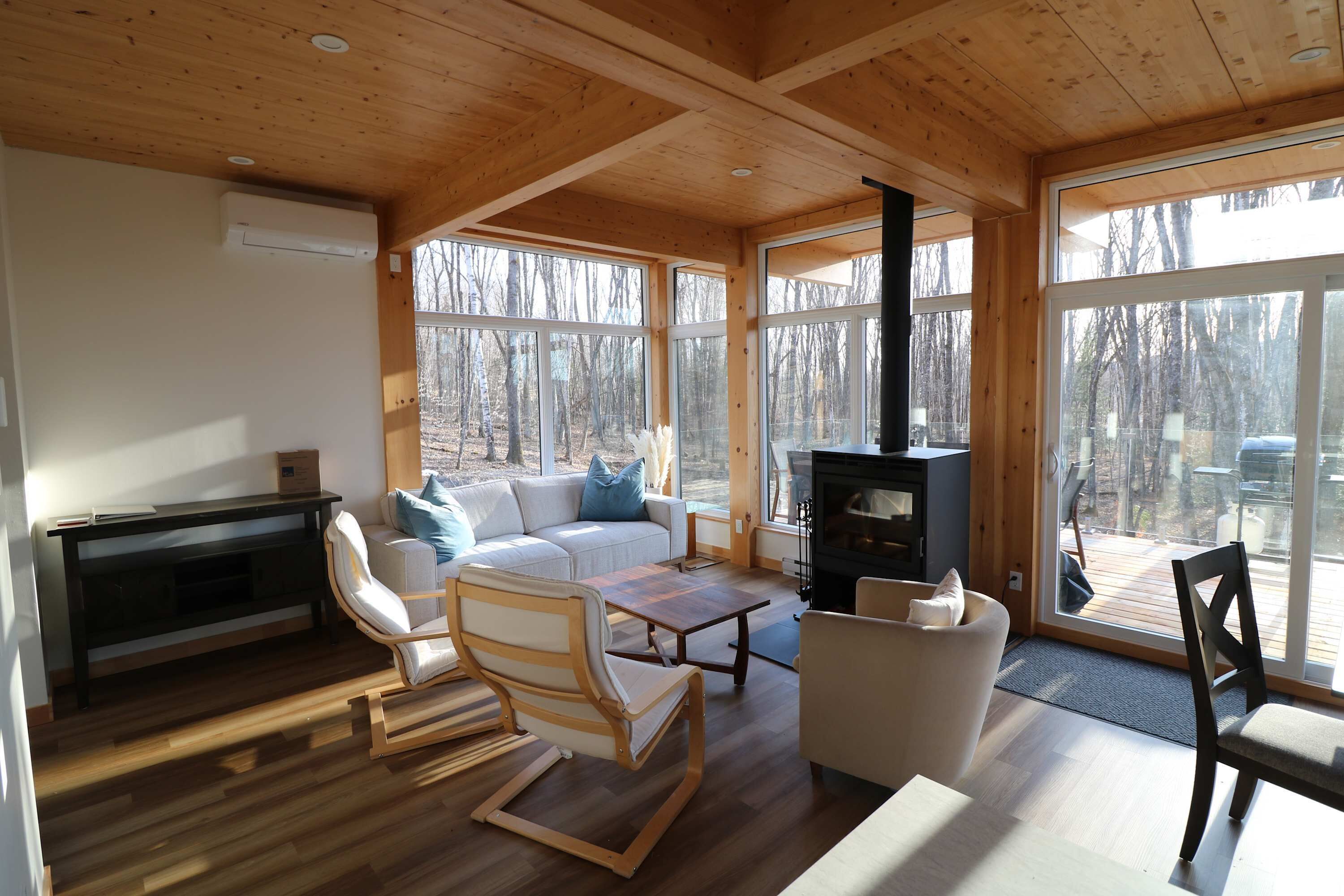 Un interior de madera con sofá, sillas, una mesa, chimenea y ventanas amplias.