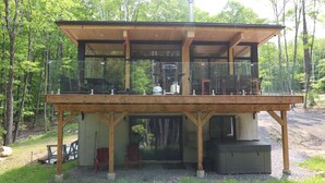 A wooden cabin with a balcony, large windows, and a gravel ground. - Lake, Spa & Game Room | Le Havre du Voyageur (La Minerve)