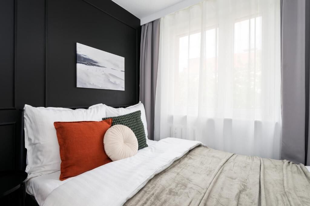 A modern bedroom with a large bed, white bedding, and a view of the outdoors through sheer curtains.
