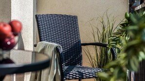 Een terras met een rieten stoel, een tafel met een fruitschaal en een bloempot.